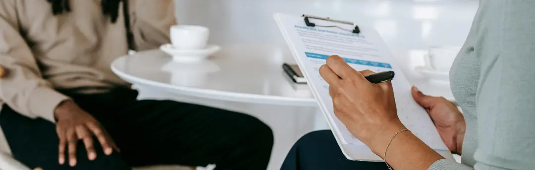 A healthcare provider takes notes on a clipboard while speaking to a patient