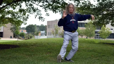 An older man in a sweatshirt and jeans practices tai chi on the Quad