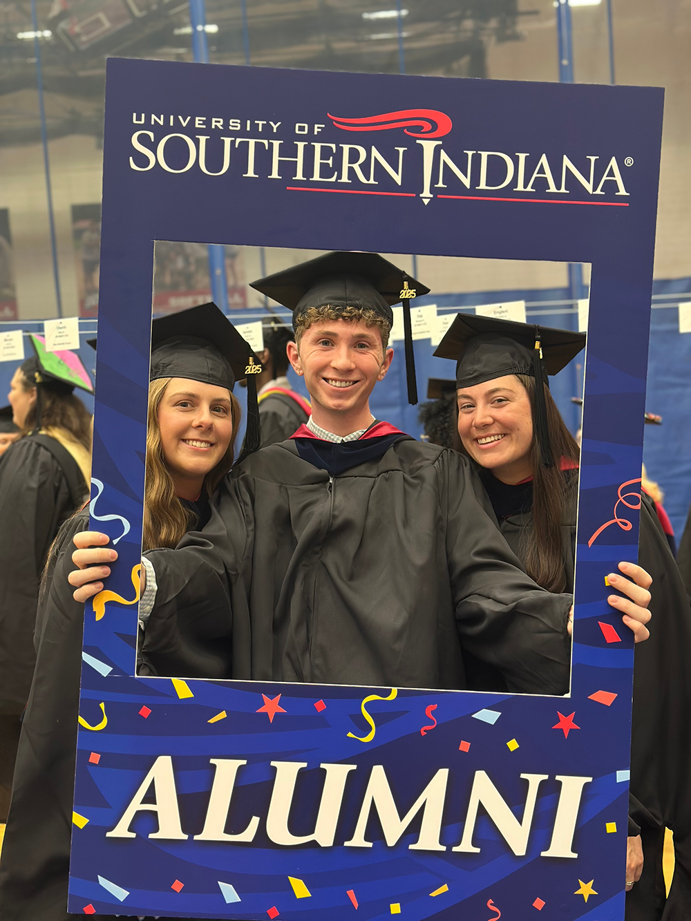 Three Occupational Therapy students wearing caps and gowns holding an alumni photo prop frame