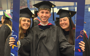 Three Occupational Therapy students wearing caps and gowns holding an alumni photo prop frame