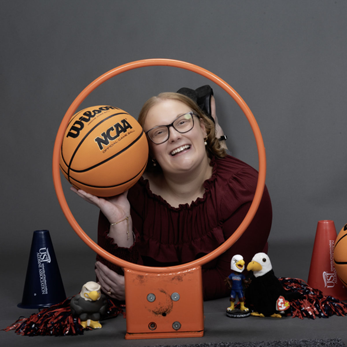 A member of the homecoming court smiles through a basketball hoop and is surrounded my little Archie Eagles, pom poms and basketball props for her homecoming photo.