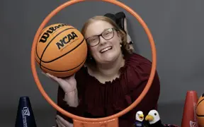 A member of the homecoming court smiles through a basketball hoop and is surrounded my little Archie Eagles, pom poms and basketball props for her homecoming photo.