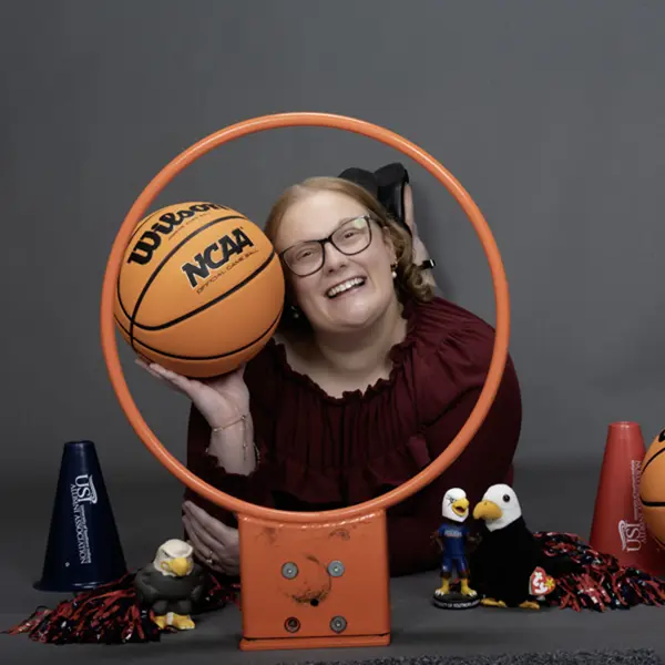 A member of the homecoming court smiles through a basketball hoop and is surrounded my little Archie Eagles, pom poms and basketball props for her homecoming photo.