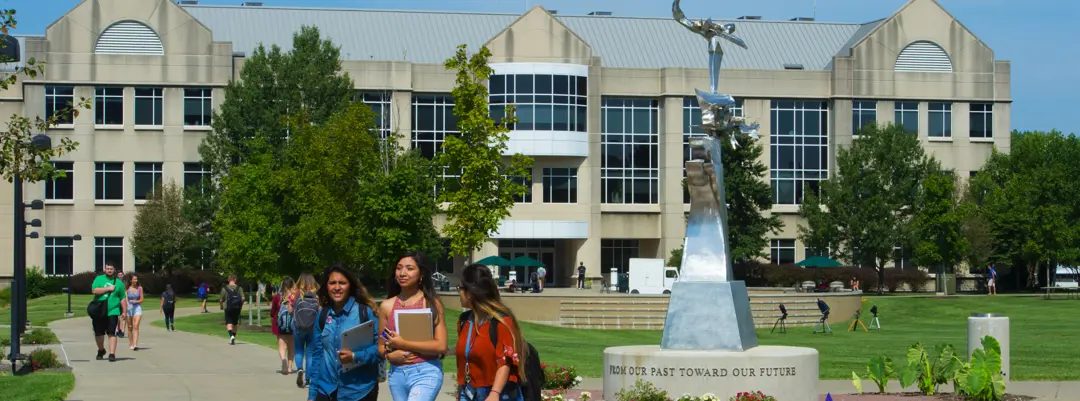 Students walk with their books and backpacks along the Quad sidewalk with the Liberal Arts Center in the background
