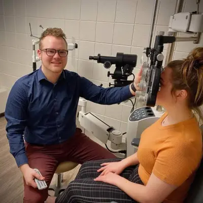 Pre-optometry student uses a phoropter machine on a practice subject