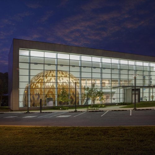 A night view of the Evansville Museum with a large gold dome inside the building, visible through glass windows.