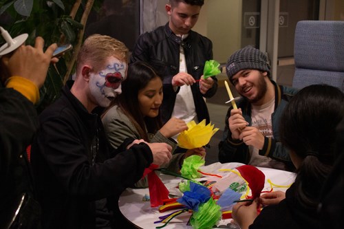 Students, one with his face painted like a Catrina, make traditional Mexican crafts