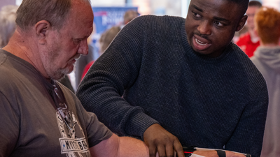 Student puts an assistive device on an older gentleman's left hand