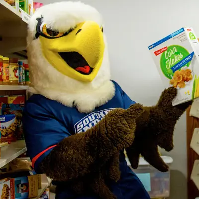 Archie mascot holding a box of cereal in the food pantry